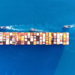 Top view Container ship full capacity approaching the port by a tugboat occupying the port International Container ship loading, unloading at sea port, Freight Transportation, Shipping,  Vessel. Logistics, import export, Transportation. Global transport business.